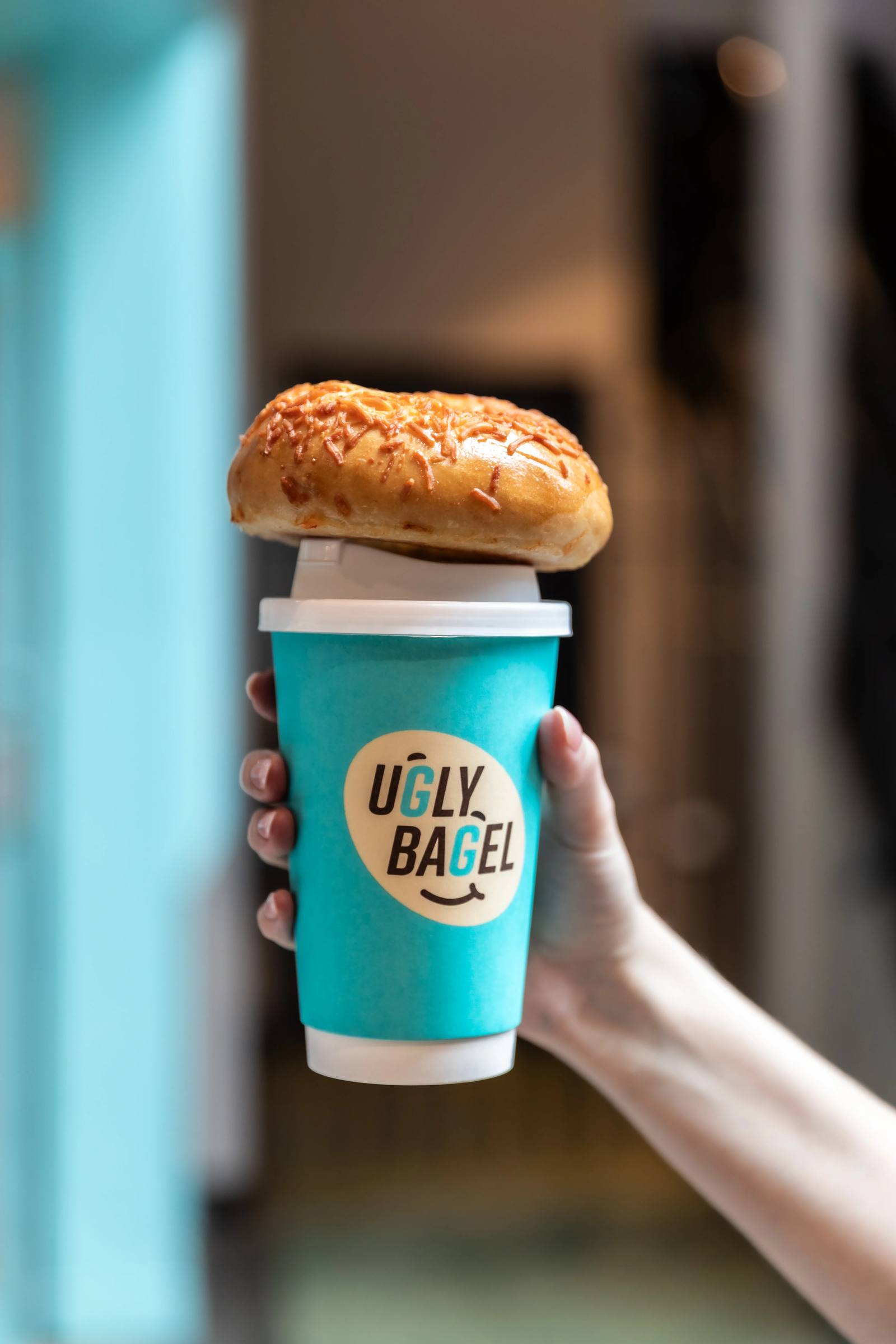 Hand holding a hot coffee with a bagel